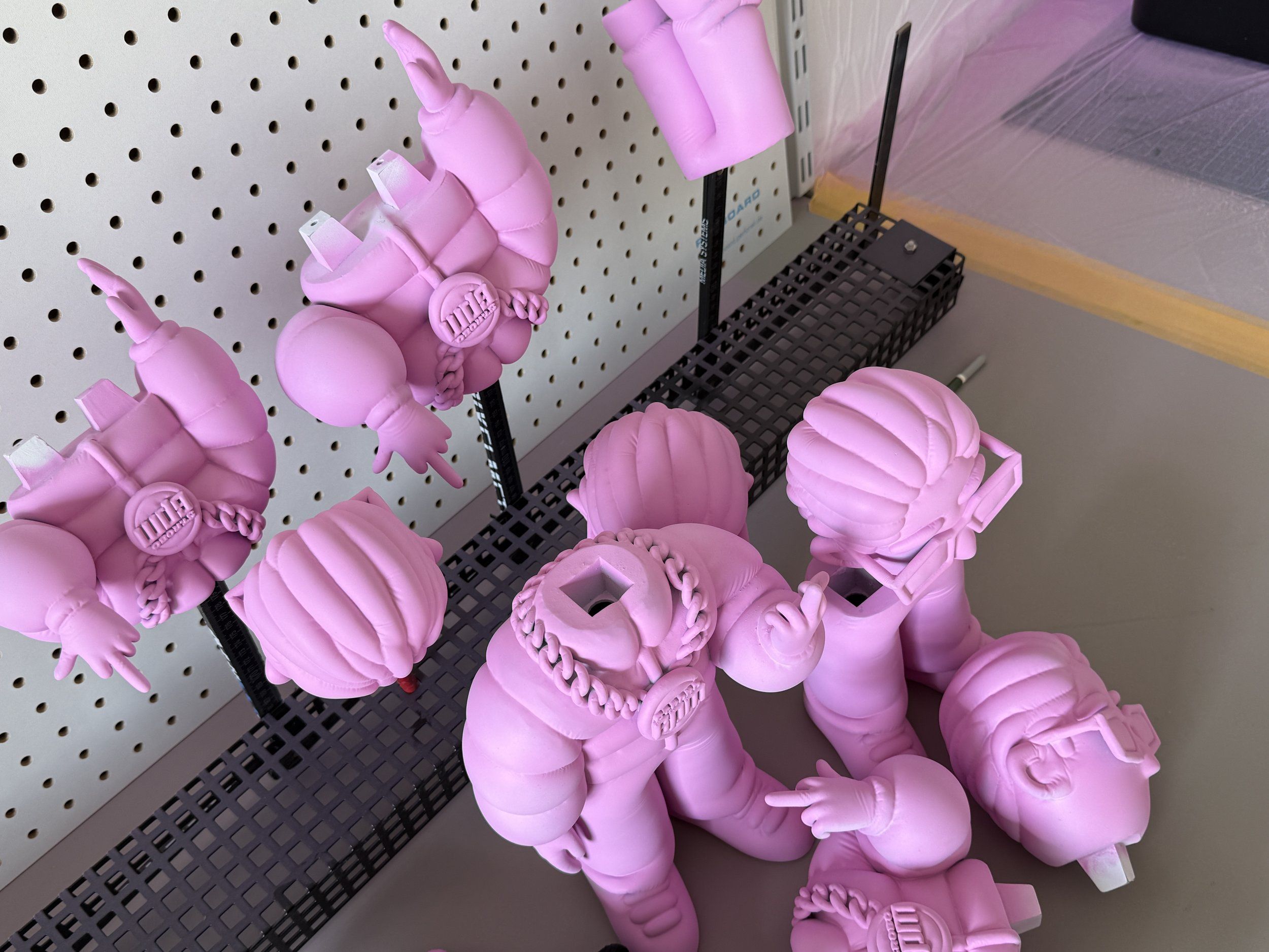 Pinke 3D-gedruckte 6PM-Figuren und Köpfe an einer Lochwand