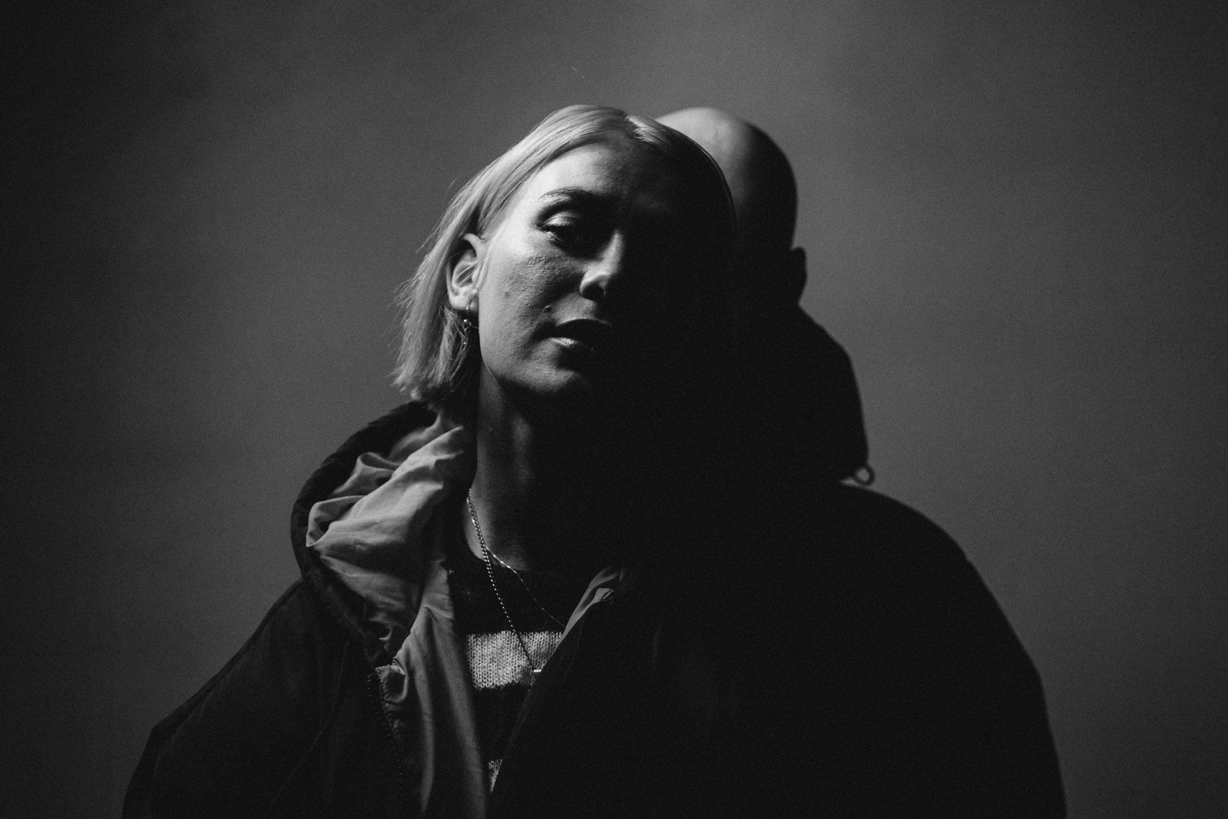 Black-and-white portrait of a woman in a hooded jacket in hard studio light
