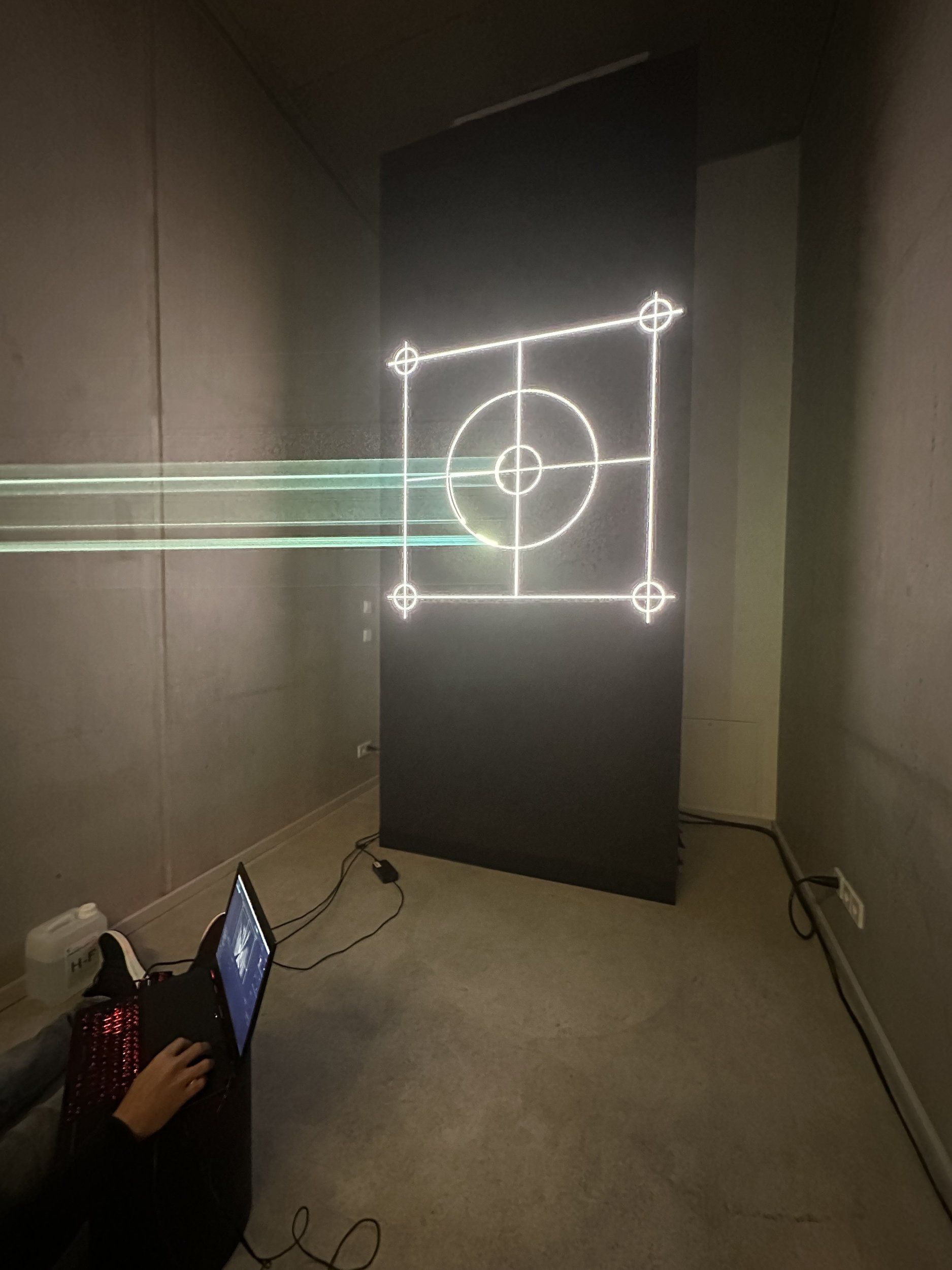 Green laser drawing a target graphic on a black LED panel in the gallery